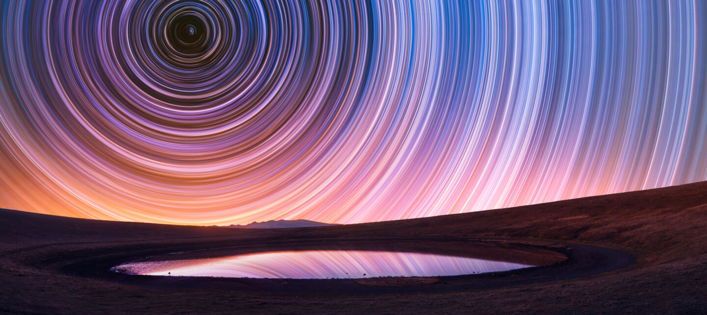 Colorful star trails over a small lake.